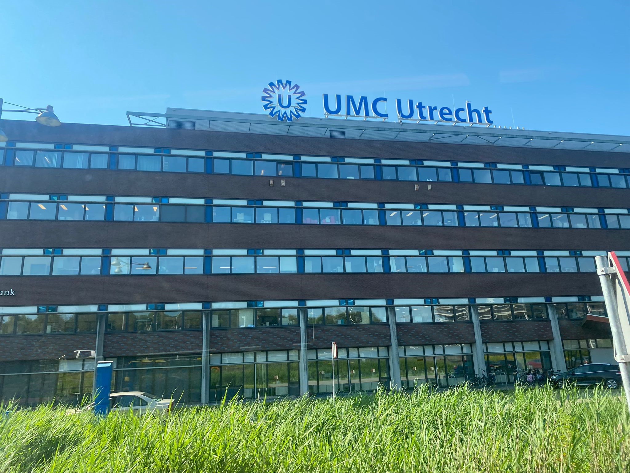 A large hospital building with a sign saying UMC Utrecht. There is green grass in front of the building